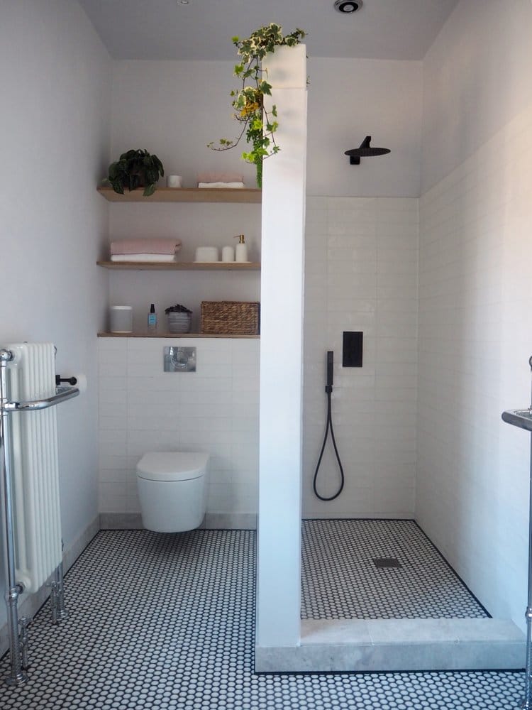 Bathroom with shower on right and toilet on left, shelves above toilet and black and white tiles on floor.