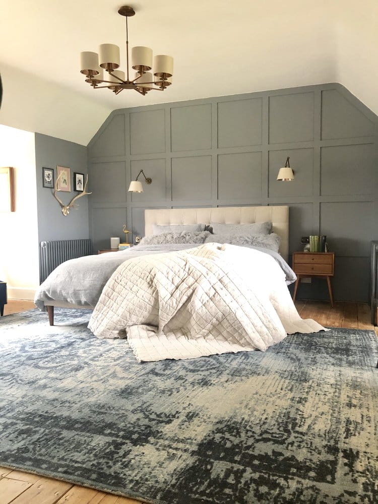 Large bedroom with grey panelled walls, large rug on floor and kingside bed with grey and white covers