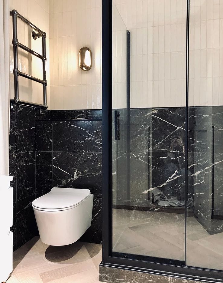 Shower and toilet with dark marble tiles on the bottom half and white tiles on the top half
